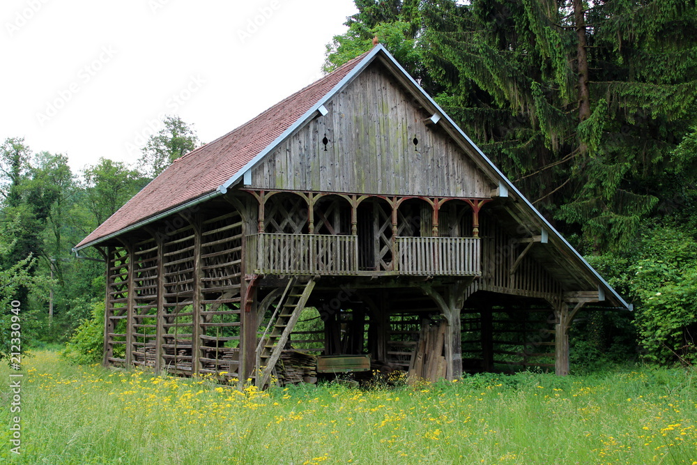 Large wooden decorated barn outdoor building surrounded with high uncut grass full of flowers, large pine trees and other vegetation Large wooden decorated barn outdoor building surrounded with high uncut grass full of flowers, large pine trees and other vegetation