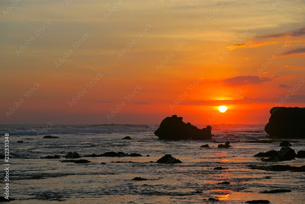 Red colors dramatic tropical sunset with black rocks silhouettes at Canggu beach, Bali, Indonesia