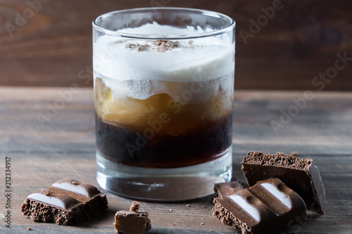 white russian cocktail with kahlua vodka and cream and chocolate pieces on wooden background