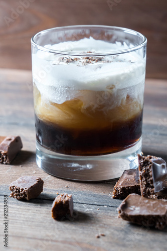 white russian cocktail with kahlua vodka and cream and chocolate pieces on wooden background
