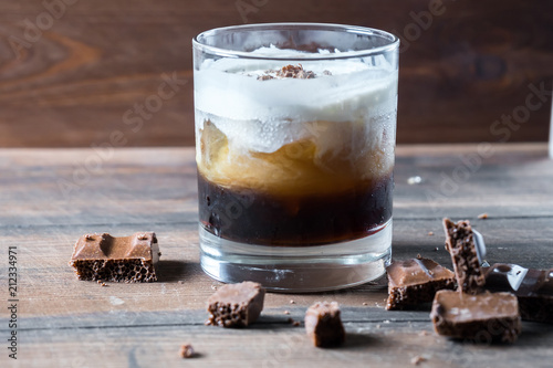 white russian cocktail with kahlua vodka and cream and chocolate pieces on wooden background