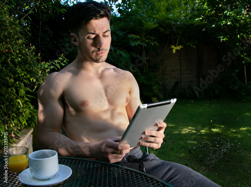 Fotografija Hunky, handsome man with pecs and six pack abs sits in garden drinking coffee an