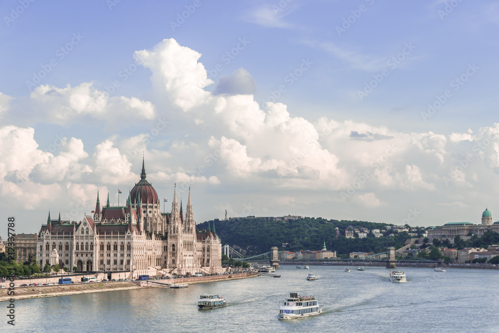 Fototapeta premium Budapest skyline with the Hungarian Parliament building, ships sailing on the Danube river and Gellert Hill under the blue cloudy sky