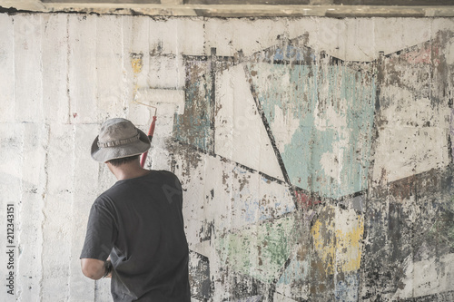 Young man clean the walls by painting white over the old cement wall.