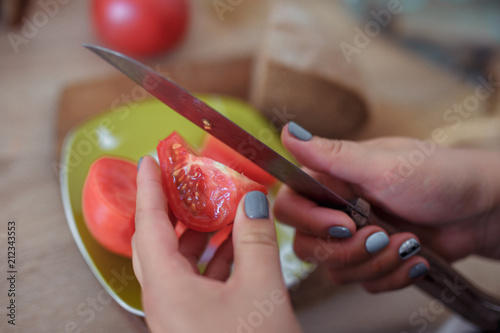sliced red tomato in women's hands on a green plate photo