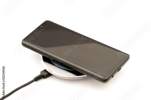 Modern black smartphone charging on wireless charger pad. Isolated on white background. Design element.