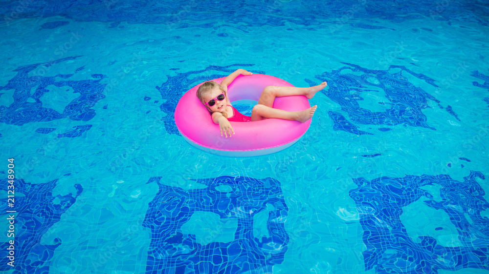 happy girl in pink rubber ring bathes in a pool