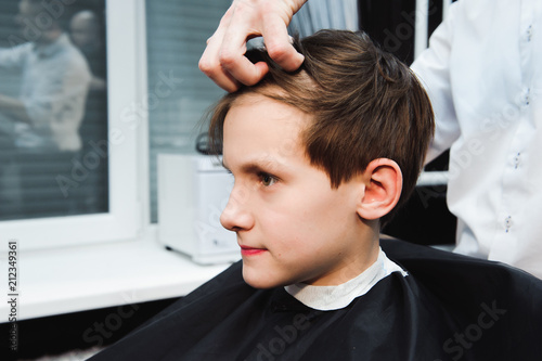 Young handsome barber making haircut of cute boy in barbershop