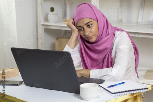 A Muslim woman wearing a hijab is tired of working in the office by the computer. Arab girl in the workplace.
