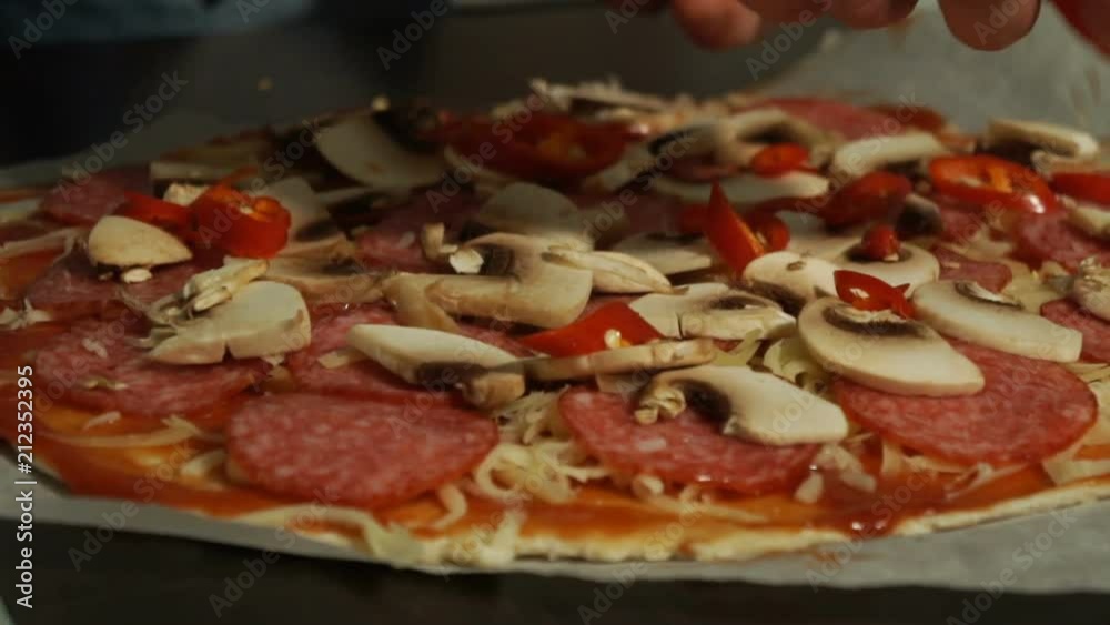 cook pours red pepper over salami and cheese on a raw pizza close-up cook pours red pepper over salami and cheese on a raw pizza close-up