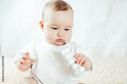 An infant plays with the pills on the bed photo