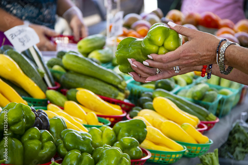 Woman with bracelets on holds two green peppers to buy at a farmer's market photo