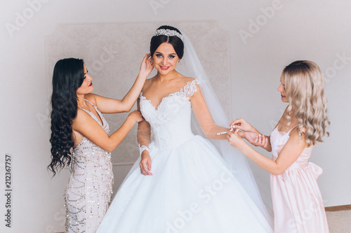 Happy bridesmaid hugging the bride in the bedroom in the morning. Before wedding ceremony. Bride preparing and wait groom. 