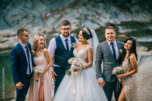 Obraz na płótnie Wedding day bride and groom with bridesmaids and groomsmen posing in sunlight evening in mountains near river gorgeous wedding newlyweds couple with best friends. People drink champagne and hugging. w salonie
