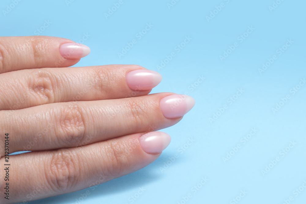 Women's hands with perfect Nude manicure. Nail Polish is a natural pale pink shade. Blue background Women's hands with perfect Nude manicure. Nail Polish is a natural pale pink shade. Blue background