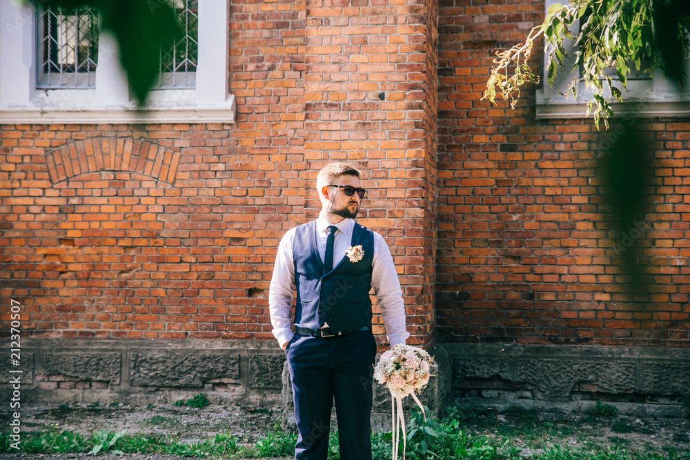 Portrait of a man near a brick wall. Groom with flowers in hand waiting bride. Portrait of a man near a brick wall. Groom with flowers in hand waiting bride.
