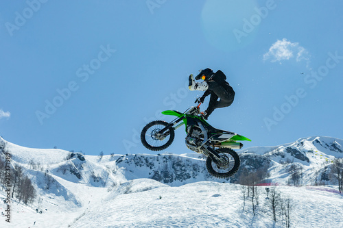 racer on a motorcycle in flight, jumps and takes off on a springboard against the snowy mountains