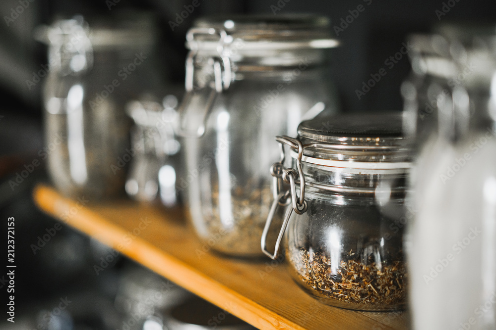 Small glass jar with a tight lid, with green tea inside, stands on a wooden shelf in a loft and rustic style. Small glass jar with a tight lid, with green tea inside, stands on a wooden shelf in a loft and rustic style.