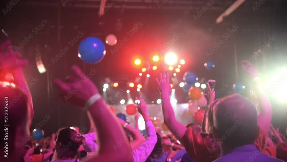 Crowd of people dancing raising hands at a concert - multi-colored balloons flying around the concert hall Crowd of people dancing raising hands at a concert - multi-colored balloons flying around the concert hall