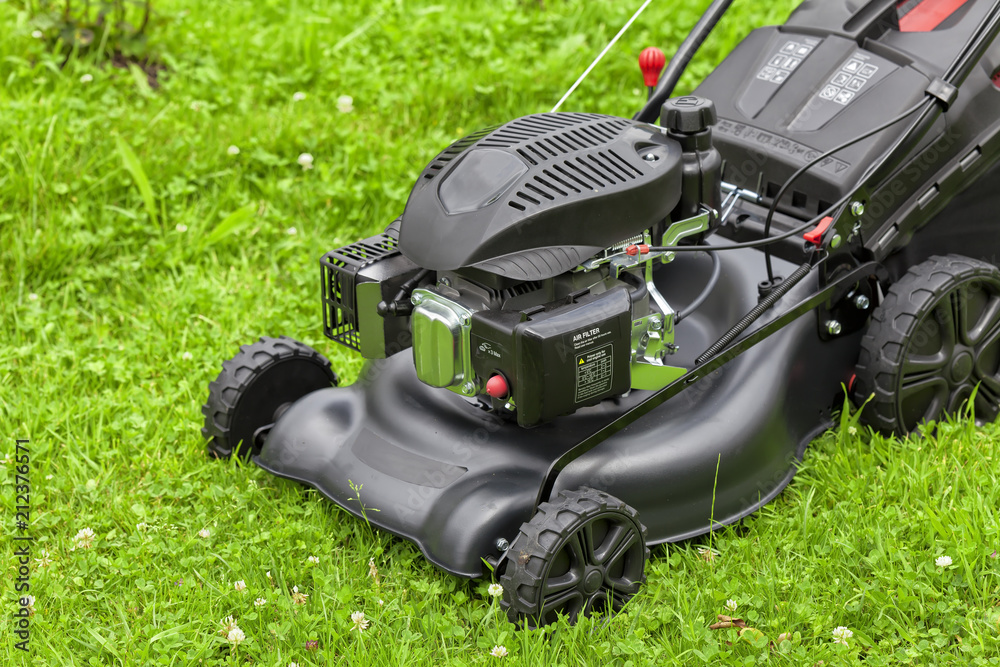 Fototapeta premium A four-stroke gasoline lawnmower on top of the grass in the garden