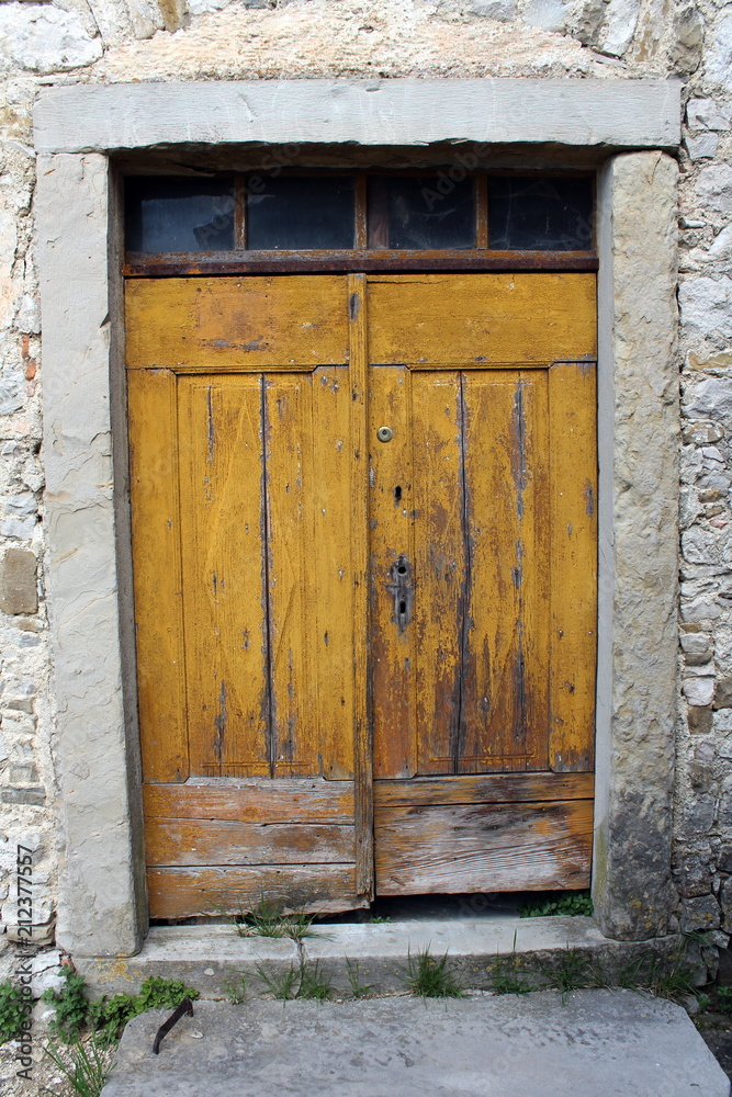 Old yellow wooden doors with small glass top windows and heavy stone frame put in traditional stone wall