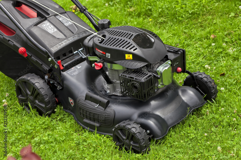 Fototapeta premium A four-stroke gasoline lawnmower on top of the grass in the garden
