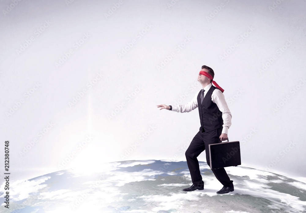 Young blindfolded businessman steps on a realistic globe Young blindfolded businessman steps on a realistic globe