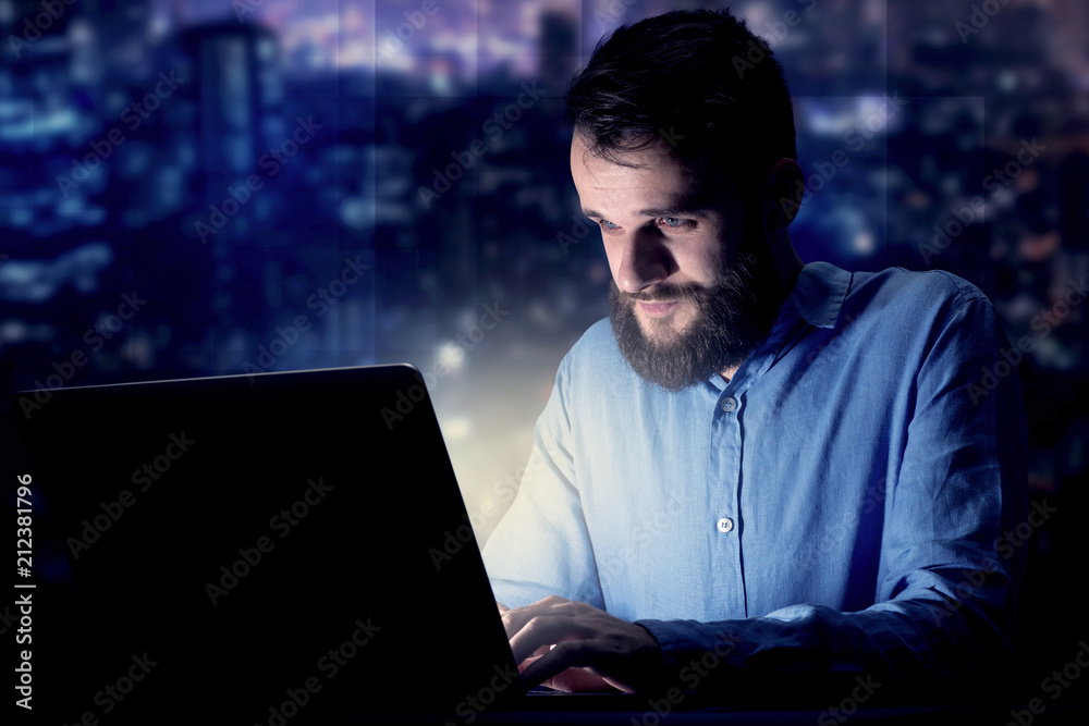 Young handsome businessman working late at night in the office with blue lights in the background Young handsome businessman working late at night in the office with blue lights in the background