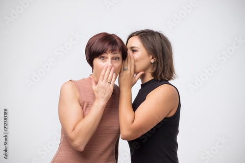 Women mother and daughter gossiping and telling a secret isolated over gray background