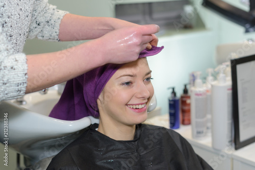 young smilingwoman having hair washed by stylist in salon sink
