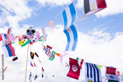 Different country flags weaving on a rope with a soccer ball in the center. Photo of a various country flags weaving on wind and blue sky on a background.