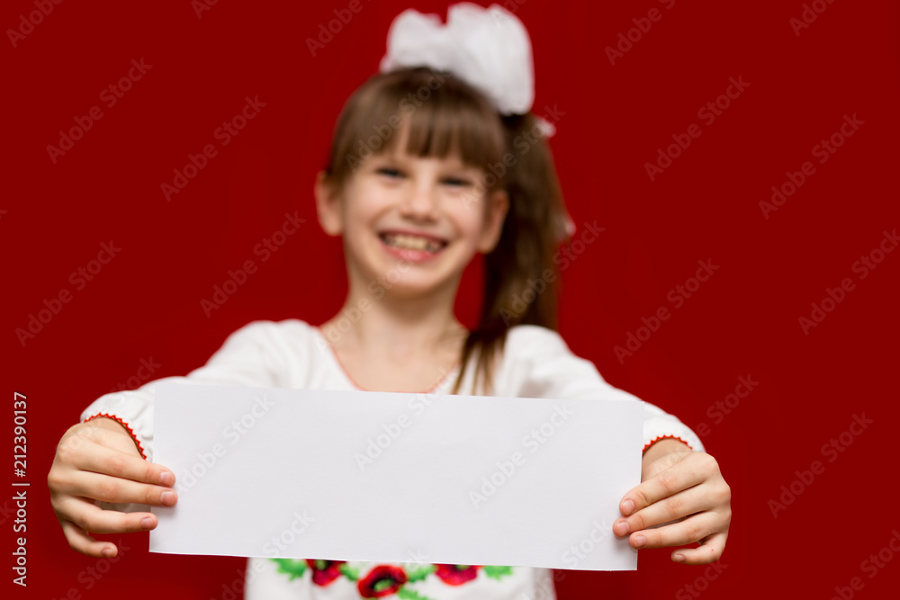 Cute smiling little girl in bow hold white blank paper on red background Cute smiling little girl in bow hold white blank paper on red background