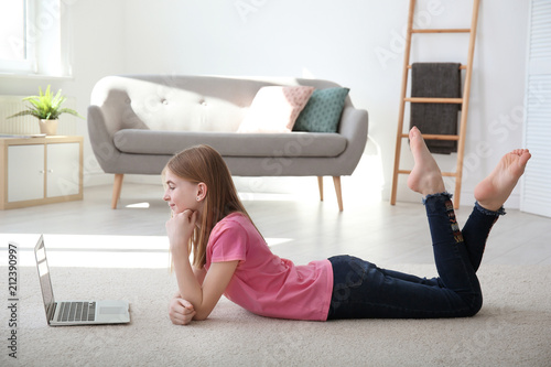 Photography Teenage girl with laptop lying on cozy carpet at home