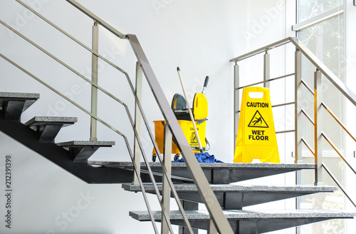 Safety sign with phrase Caution wet floor and mop bucket on stairs. Cleaning service