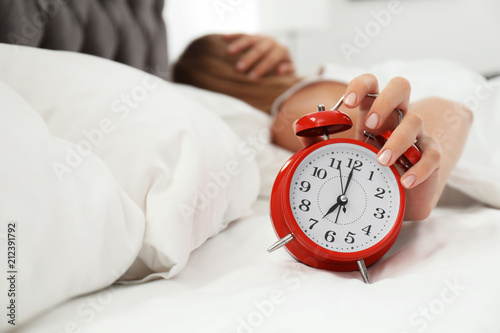 Woman turning off alarm clock in bedroom