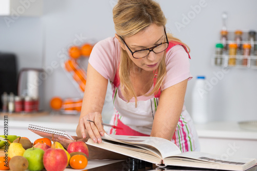 mature woman reading cookbook in the kitchen looking for recipe