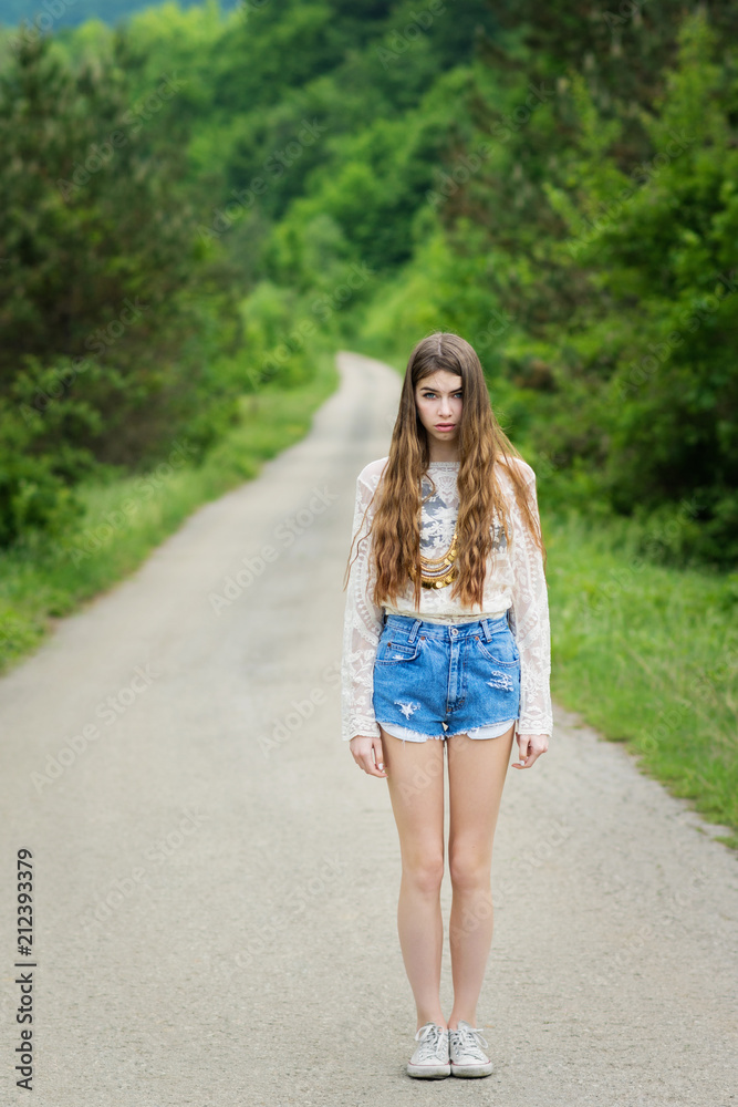 Young woman in casual summer outfit standing on the street among trees. Loneliness or depression concept. Young woman in casual summer outfit standing on the street among trees. Loneliness or depression concept.