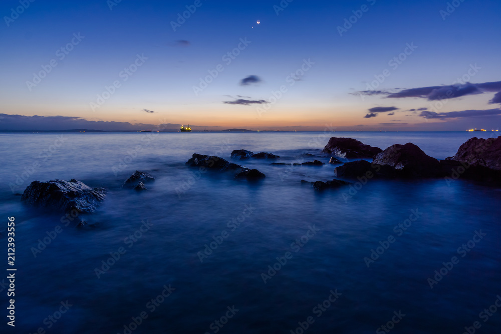 Obraz premium 夜明けの三日月と金星が輝く磯で