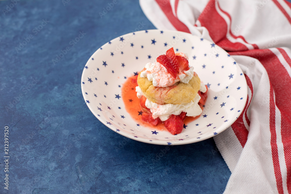 Homemade Strawberry Shortcake in White Bowl with Blue Stars; Red and White Striped Towel; Blue Background