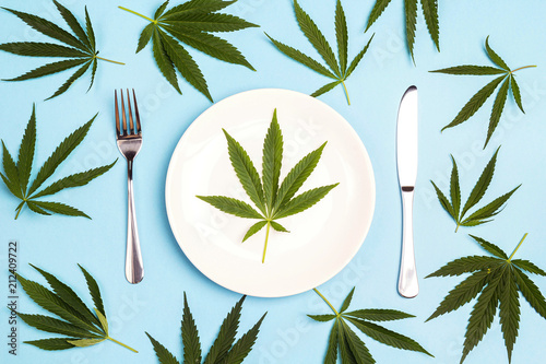 Medical concept table setting with cutlery and cannabis leaves on blue background.