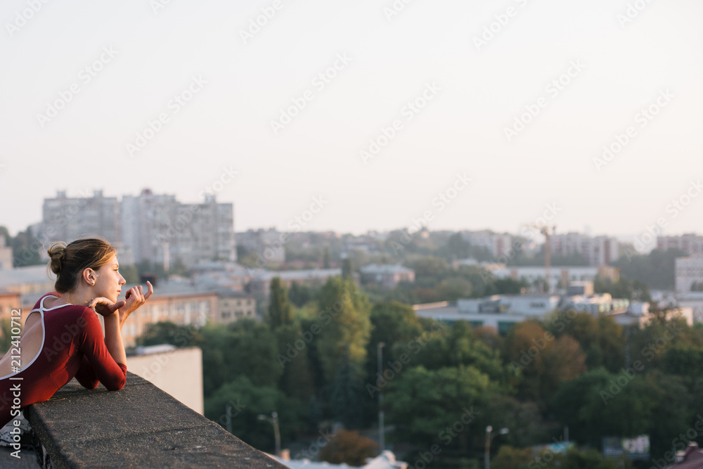 Young and graceful ballerina contemplating sunset cityscape from the roof of city building