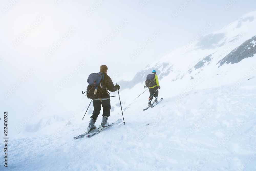Two men skiing together on the snow mountains on a foggy day.
