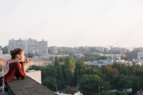 Young and graceful ballerina contemplating sunset cityscape from the roof of city building