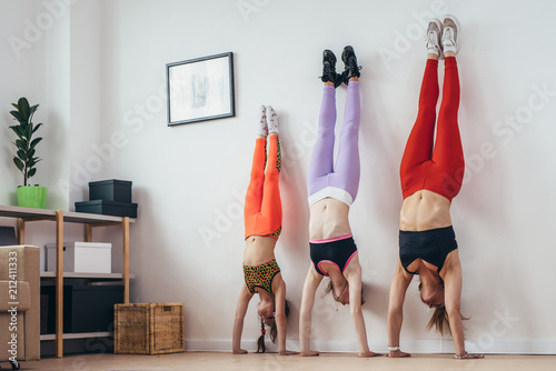 Females doing handstand pose near wall. Mother and daughters exercising at home, sport, family photo