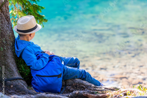 A boy of 8 years with a backpack resting by the lake in the Tatras