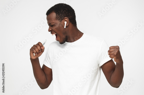 Young handsome african american man singing his favorite song, wearing blank white t shirt, isolated on gray background
