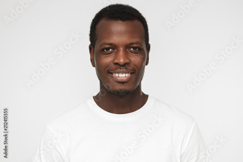Close up shot of smiling attractive african american man in blank white t-shirt isolated on gray background
