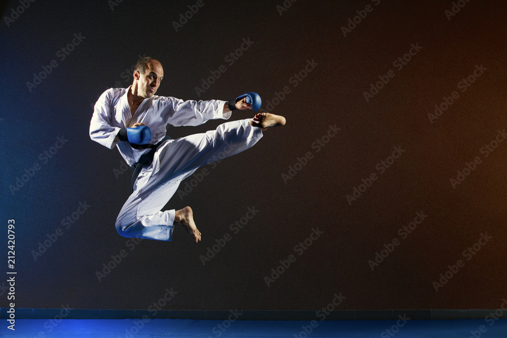 A man with blue overlays on his hands beats a kick in a jump