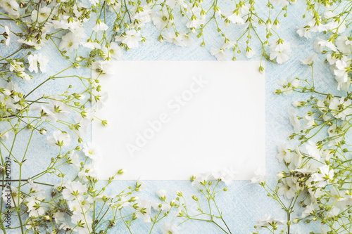 Empty sheet of paper surrounded by small white flowers. Blank postcard on a blue background