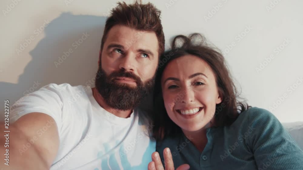 Modern stylish parents lying in bed and recording video, smiling, actively gesticulating, talking to their followers. Social networks, blogging, popularity. Lazy morning, cool parents. Modern stylish parents lying in bed and recording video, smiling, actively gesticulating, talking to their followers. Social networks, blogging, popularity. Lazy morning, cool parents.
